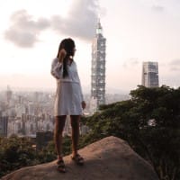 A woman in the foreground poses in front of the Taipei 101 skyscraper, which looms over the city of Taipei, Taiwan